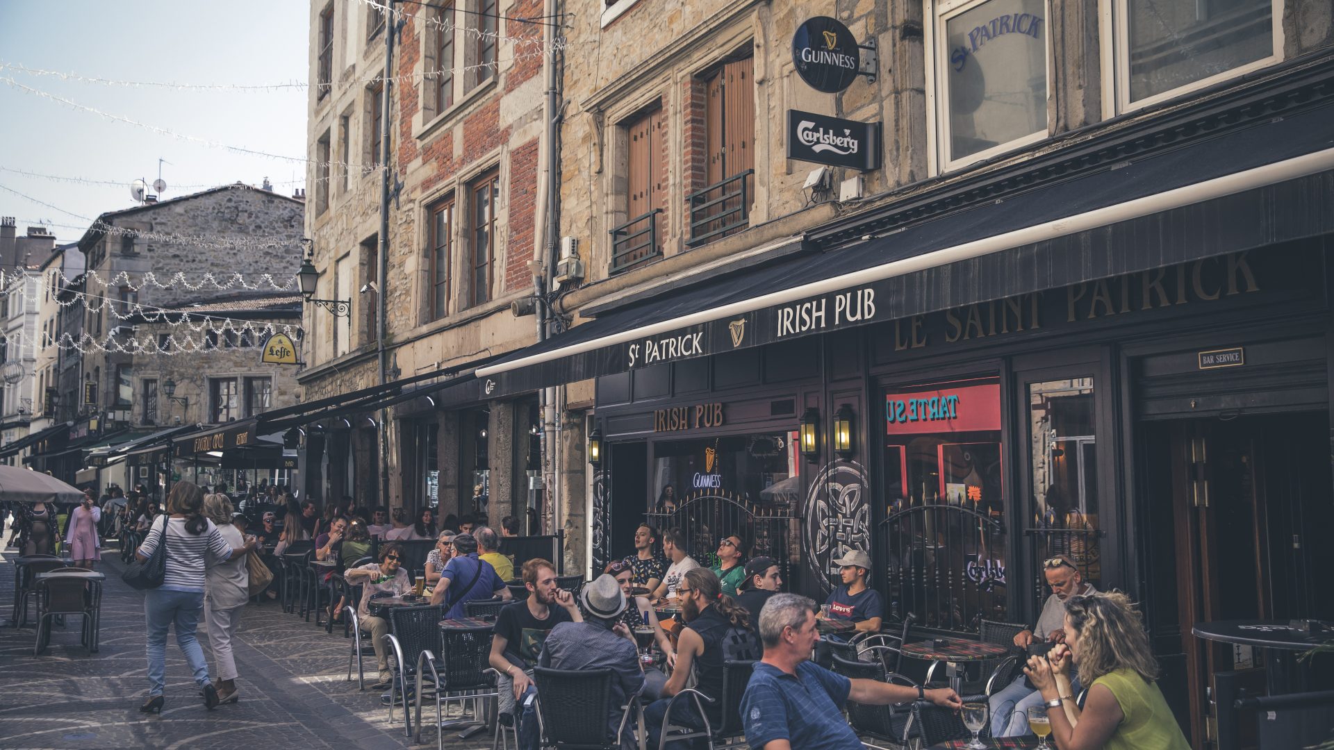Fête de la Saint-Patrick à Saint-Étienne : des personnes assises en terrasse devant la façade en pierre et briques du Saint-Patrick Irish Pub, à Saint-Étienne.